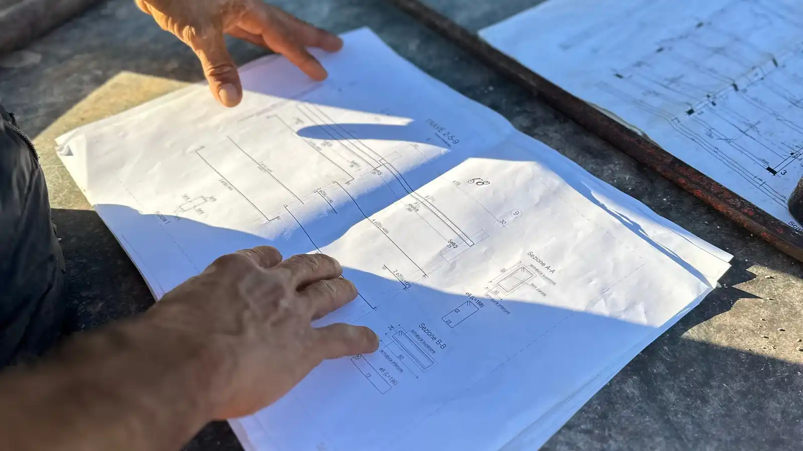 A pair of hands reviewing architectural blueprints for an outdoor building project