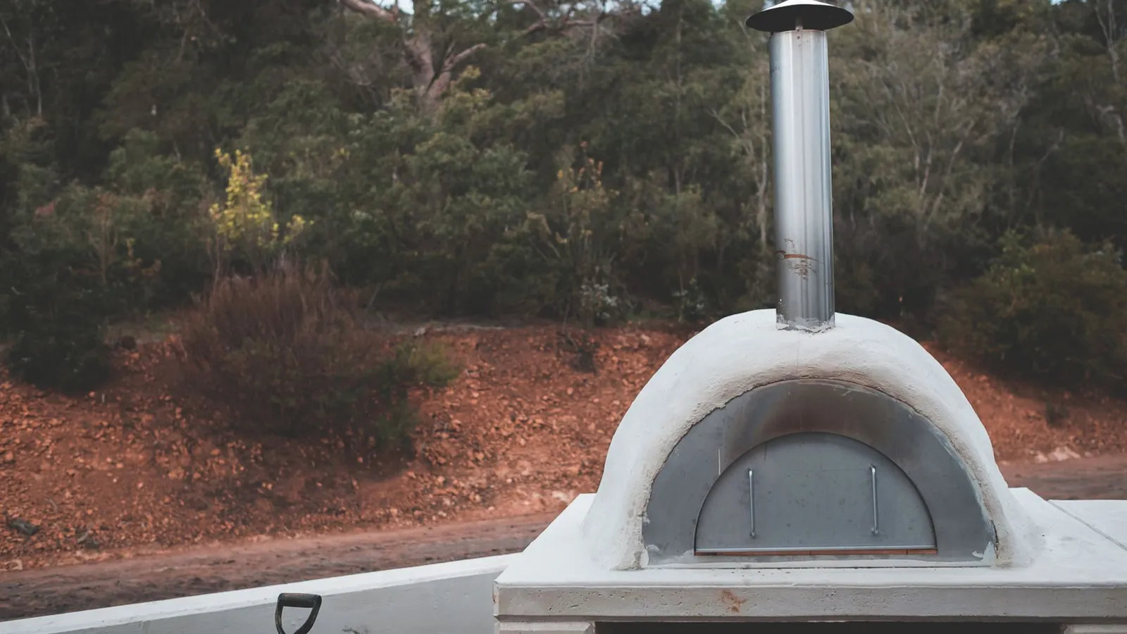 Stone and stucco pizza oven with metal chimney in a backyard bbq area