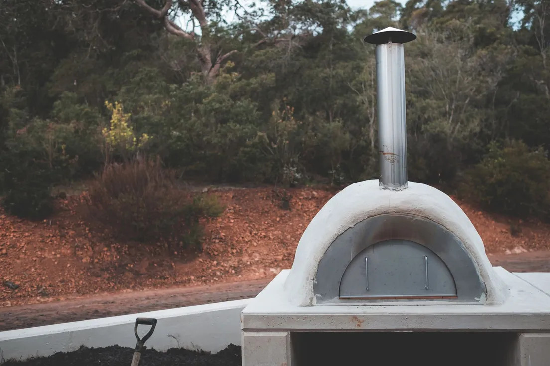 Stone and stucco pizza oven with metal chimney in a backyard bbq area