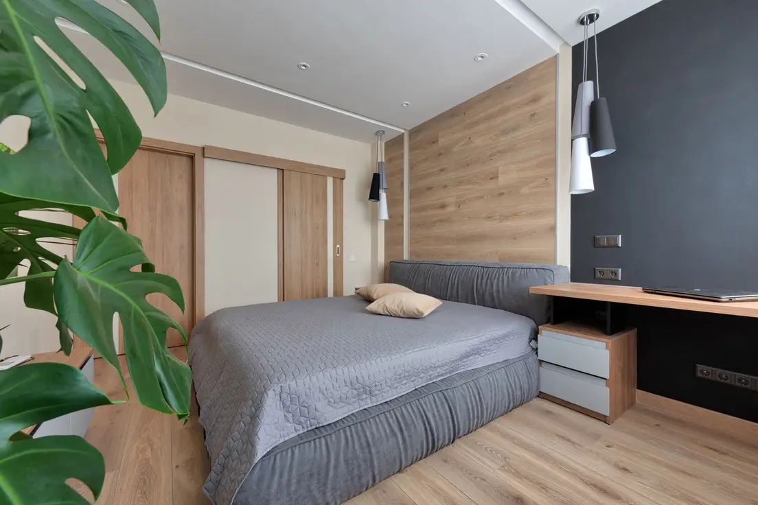A large monstera plant in the corner of a bedroom with wood paneling and a charcoal accent wall
