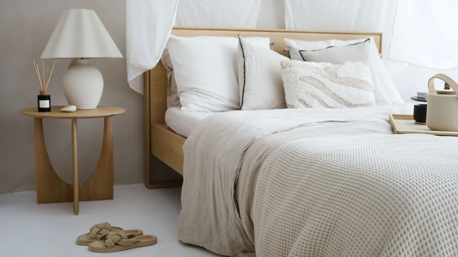 A low wood platform bed with white linen bedding under a sheer canopy curtain