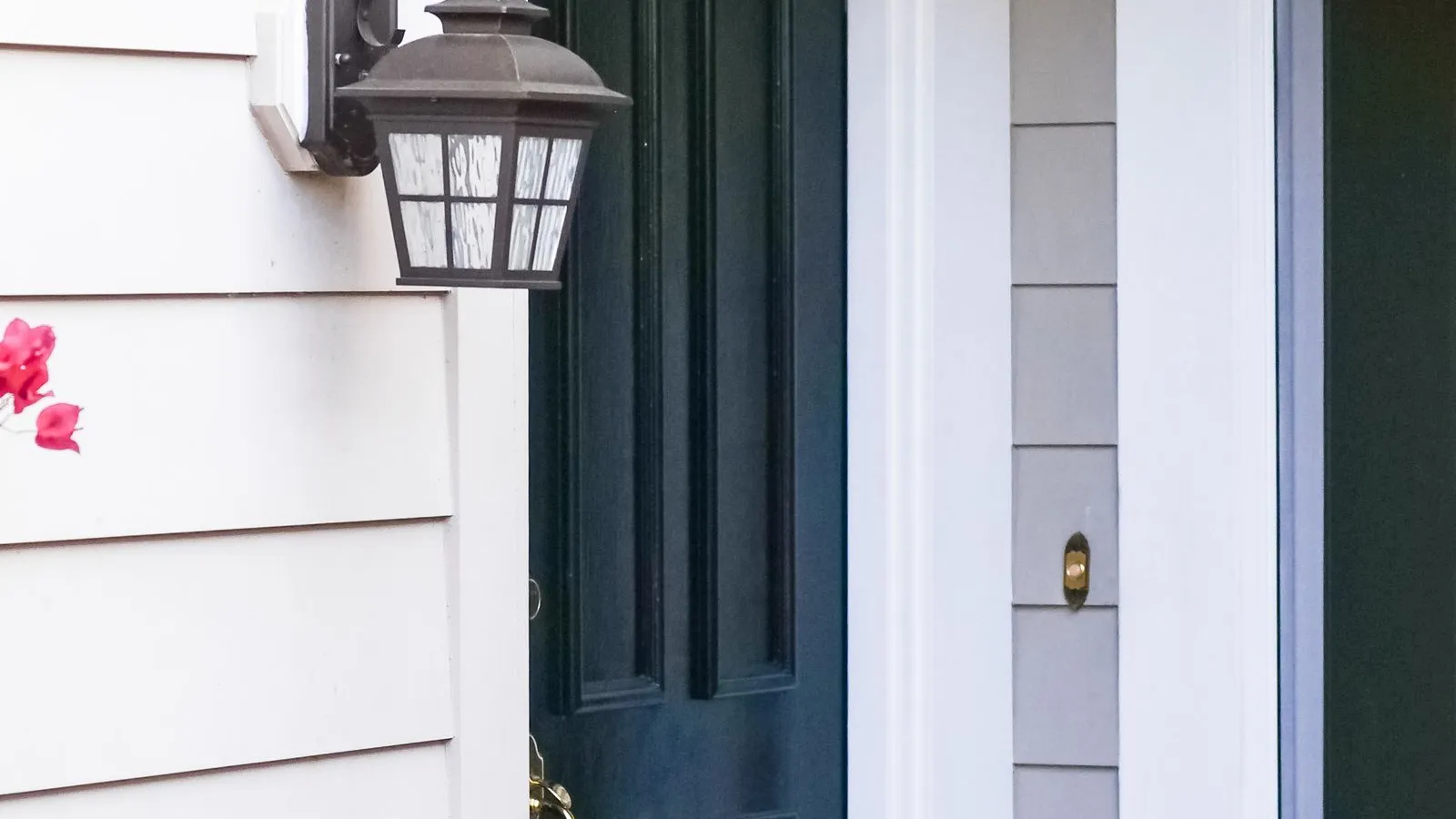 A black outdoor wall sconce mounted beside a dark green front door