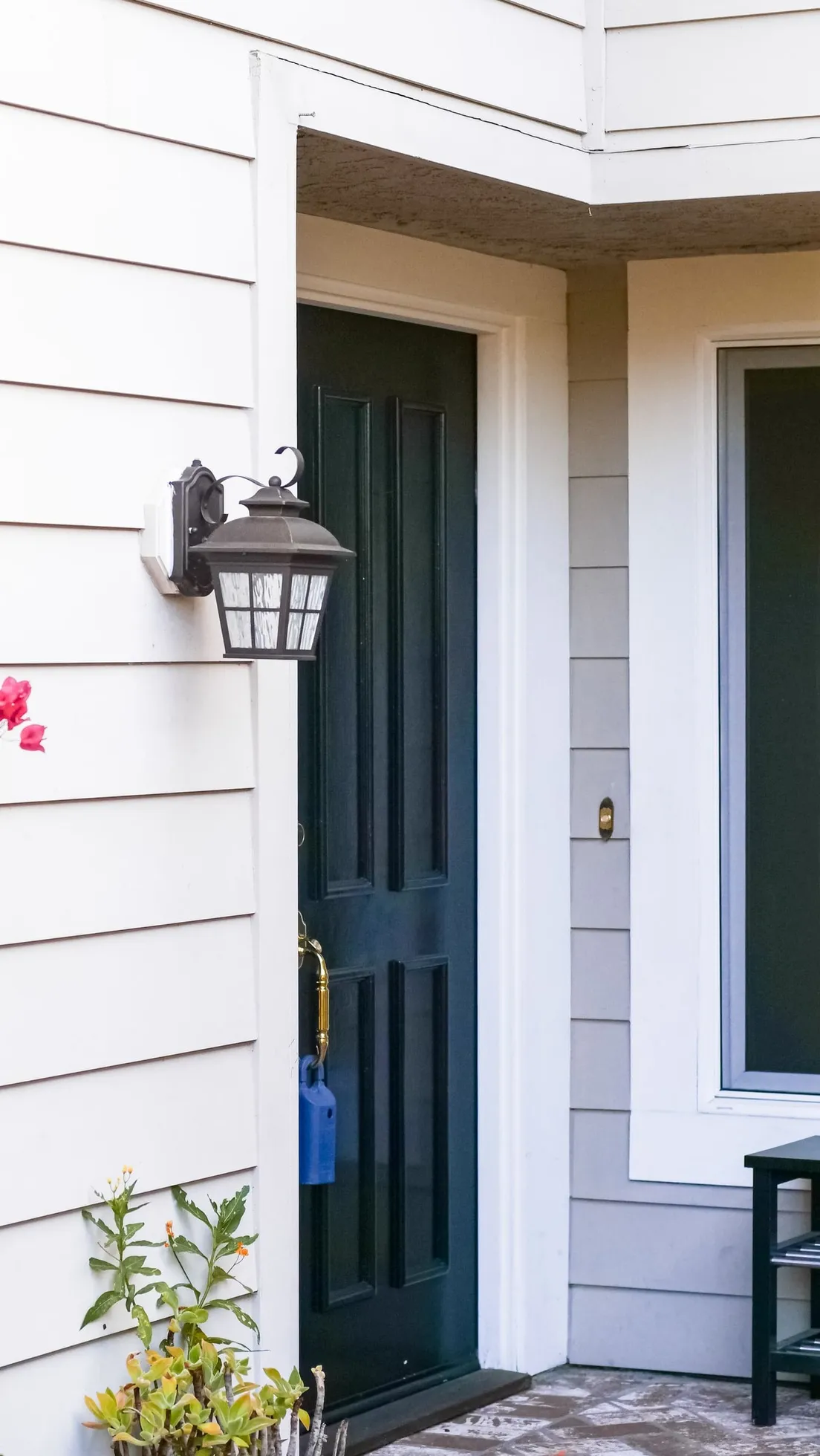 A black outdoor wall sconce mounted beside a dark green front door