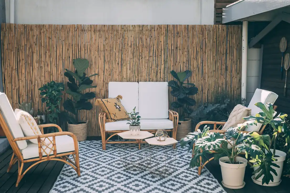 A cozy balcony seating area backed by a tall bamboo privacy screen with potted plants