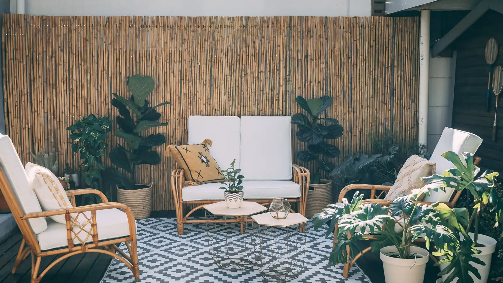 A cozy balcony seating area backed by a tall bamboo privacy screen with potted plants