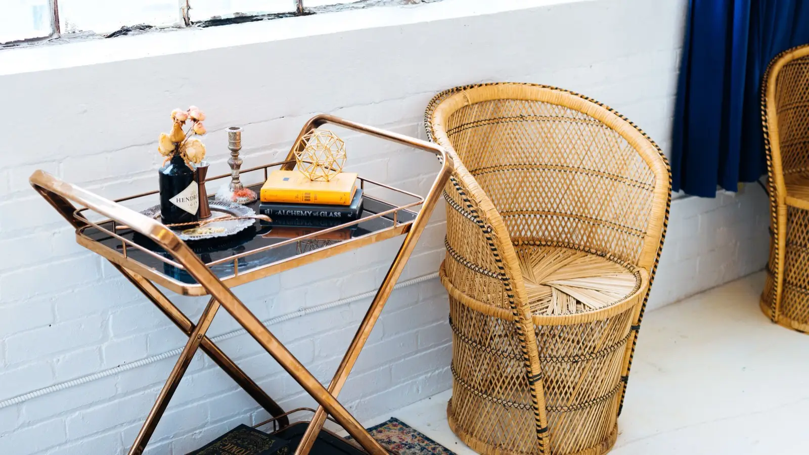 A woven rattan barrel chair next to a brass bar cart with books and dried flowers