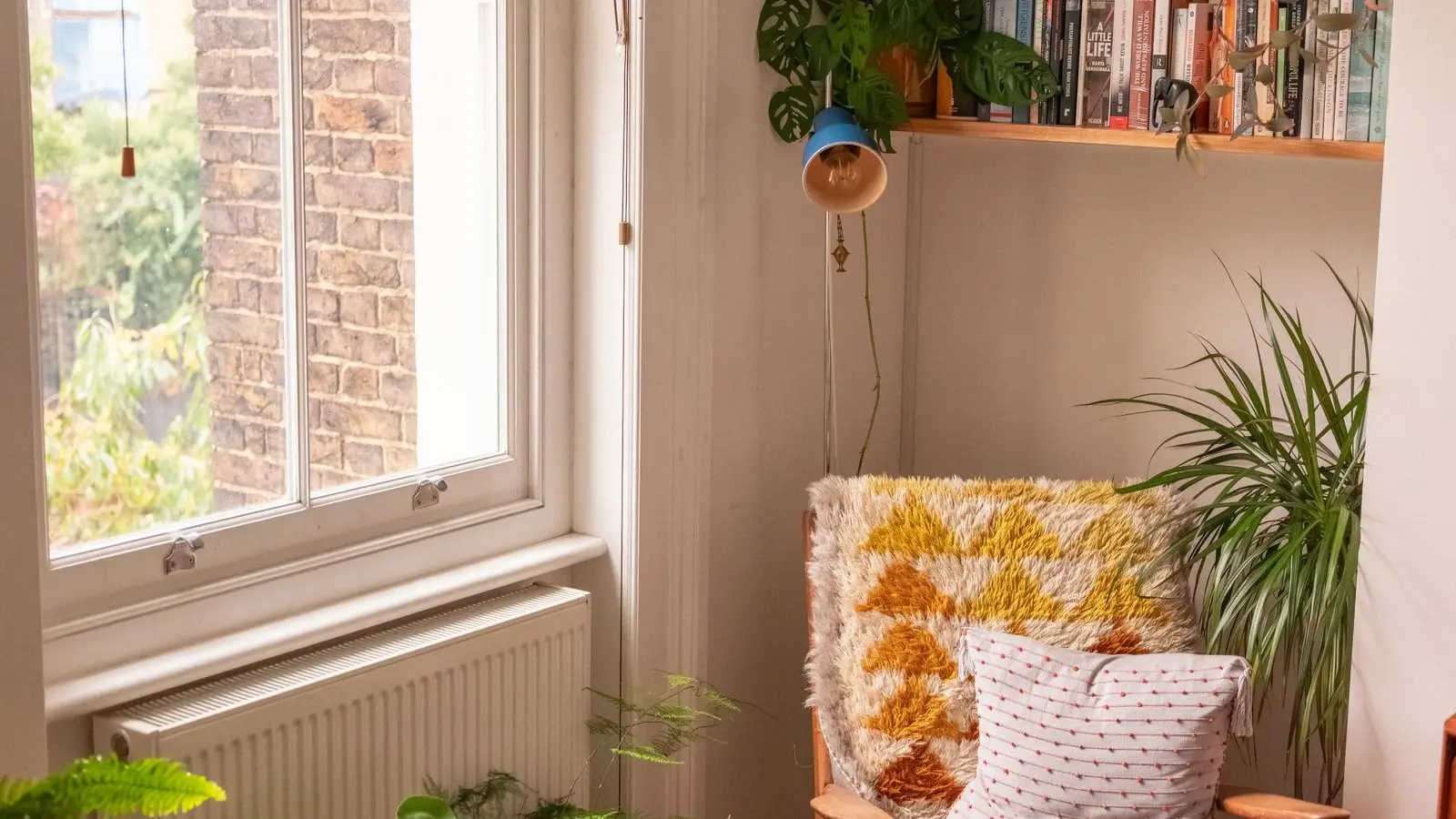 A reading nook with an armchair, potted plants, and a bookshelf by a window