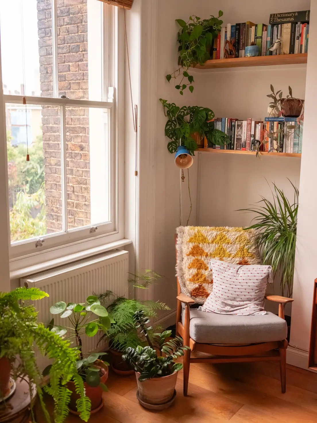A reading nook with an armchair, potted plants, and a bookshelf by a window