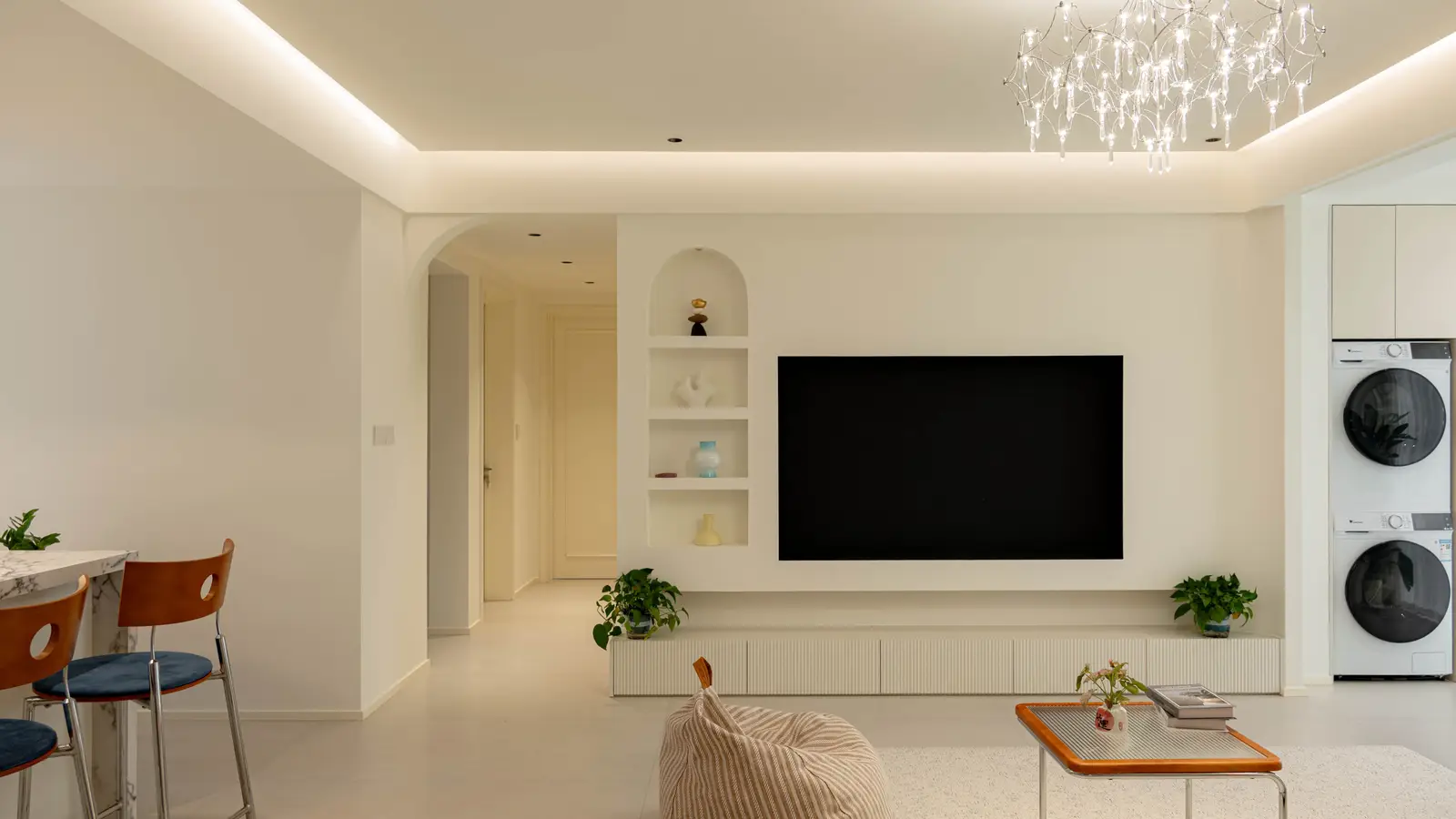 A TV recessed flush into a white living room wall next to an arched decorative shelving niche