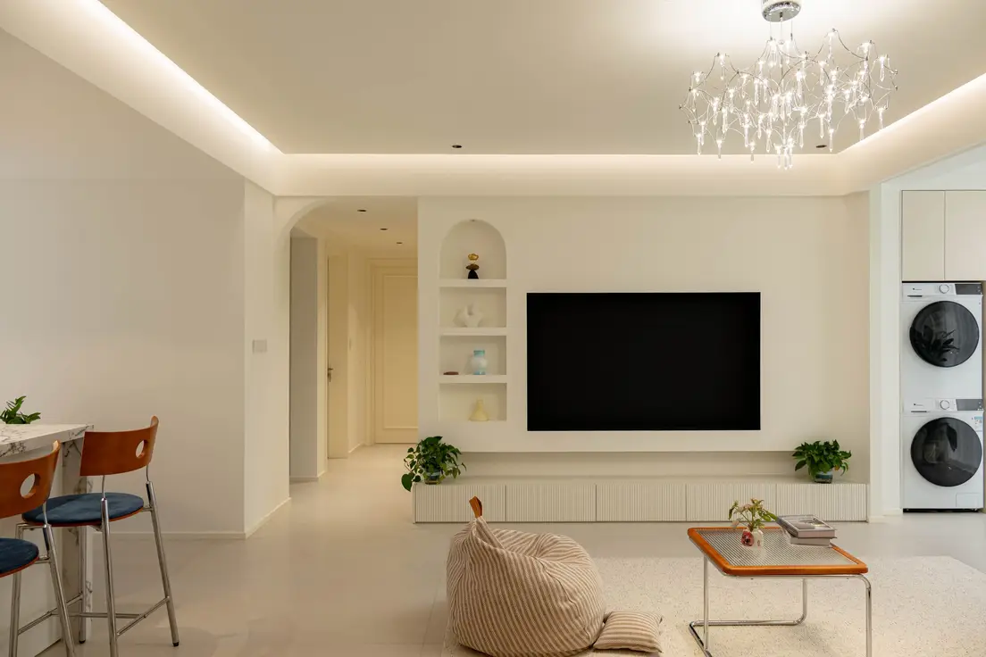A TV recessed flush into a white living room wall next to an arched decorative shelving niche