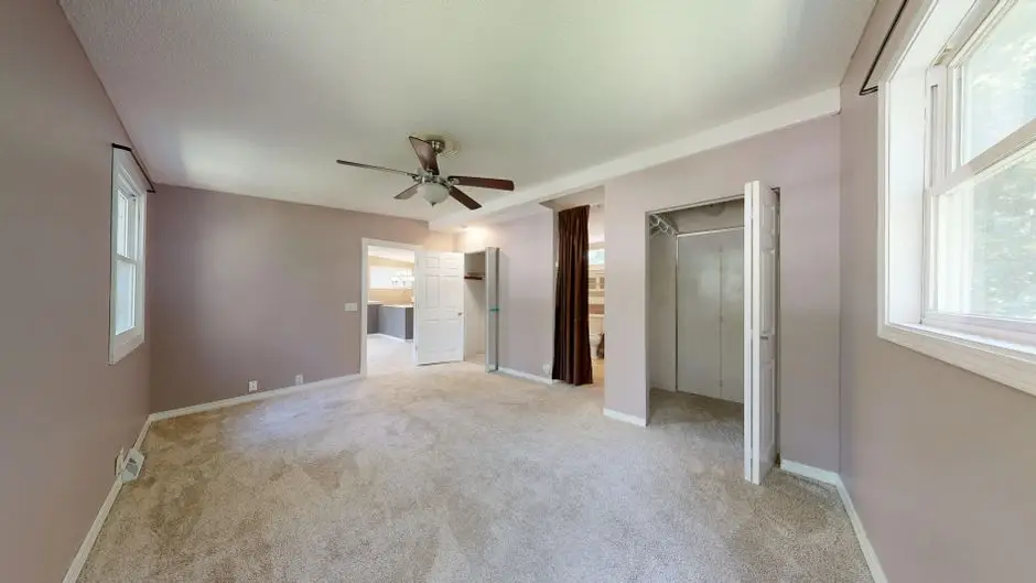 A spacious empty bedroom with neutral wall color and natural light from multiple windows, staged for a home sale