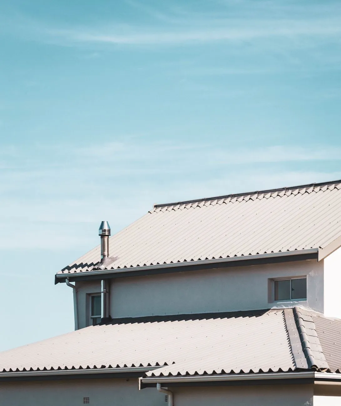 A close-up of a house roofline with tiled shingles and matching light-colored fascia trim