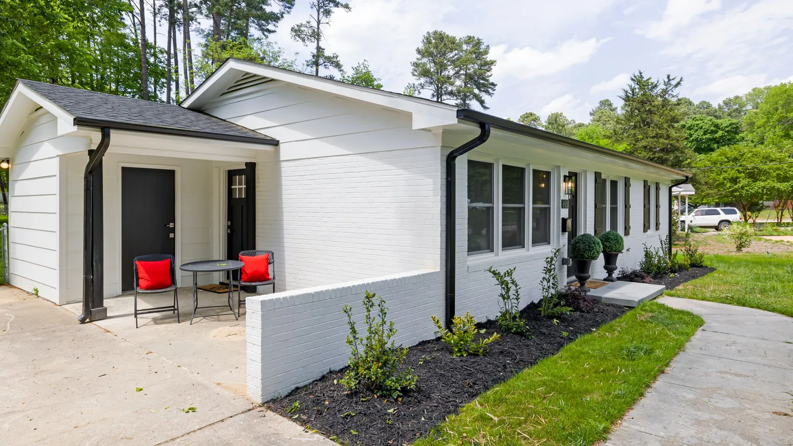A white brick house exterior with a matching black door, shutters, and gutter downspout