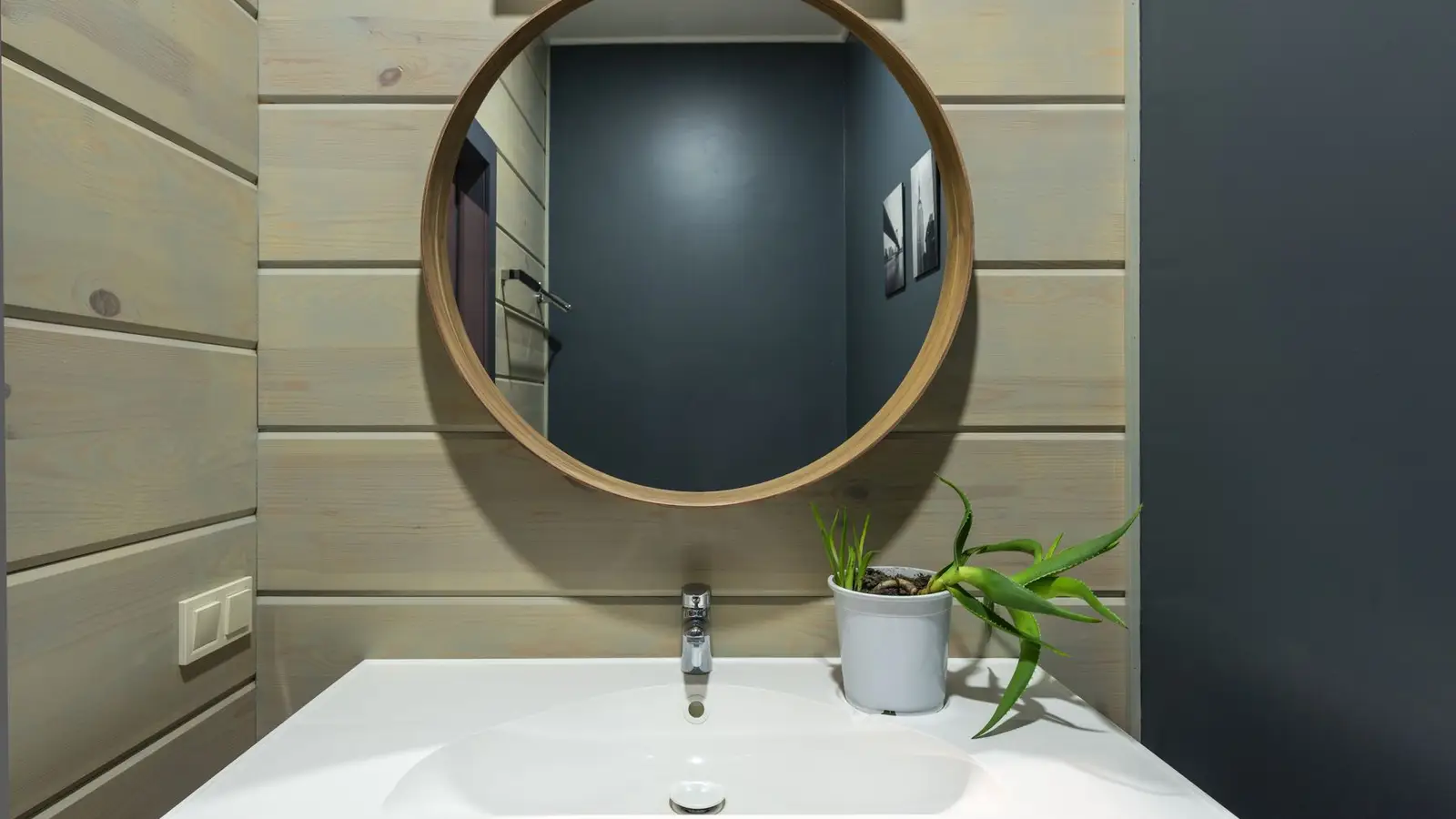 A round wood-framed mirror hanging above a small bathroom sink with a potted plant