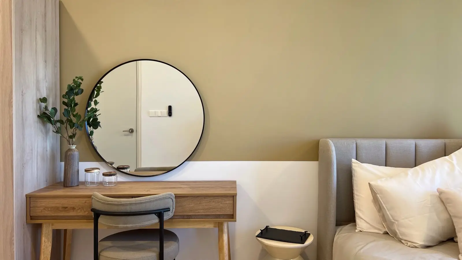 A large round black-framed mirror above a wood vanity desk with a faux plant