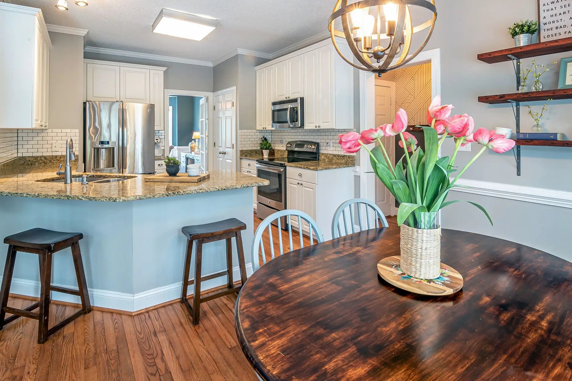 A round wood dining table with white chairs in a small kitchen nook