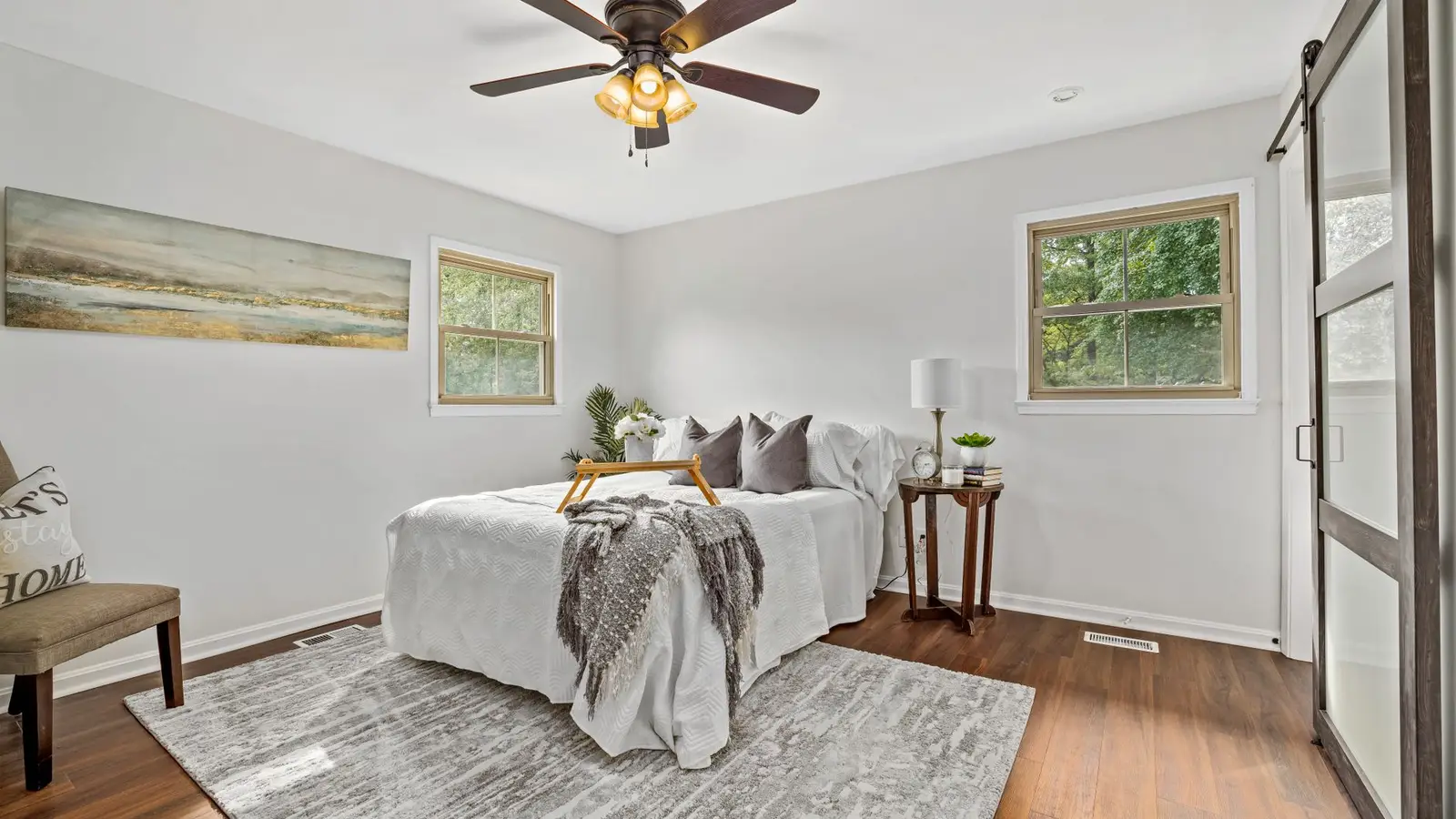 A gray patterned area rug under a bed in a small bedroom with a barn door and ceiling fan