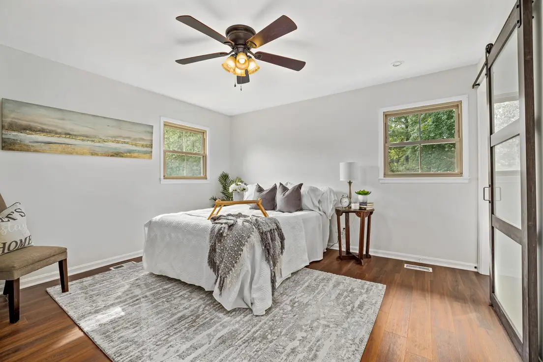 A gray patterned area rug under a bed in a small bedroom with a barn door and ceiling fan
