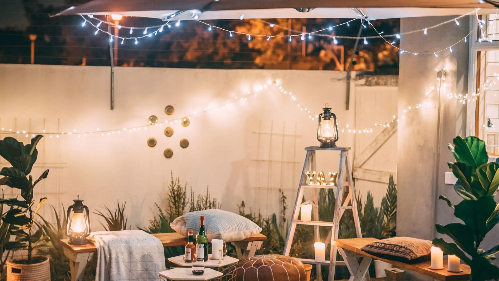 A geometric black and white outdoor rug laid on a wood deck with poufs and string lights above