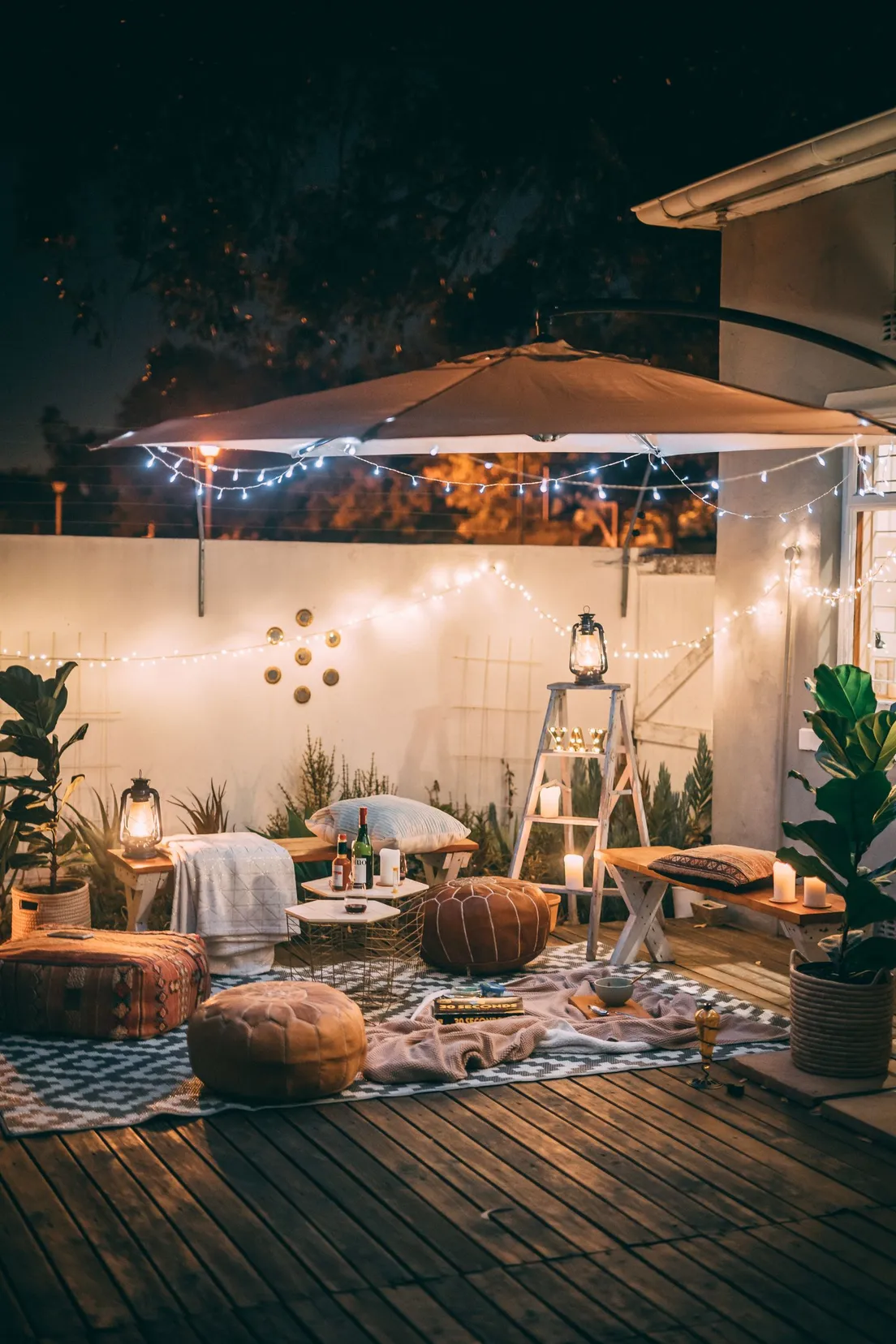 A geometric black and white outdoor rug laid on a wood deck with poufs and string lights above
