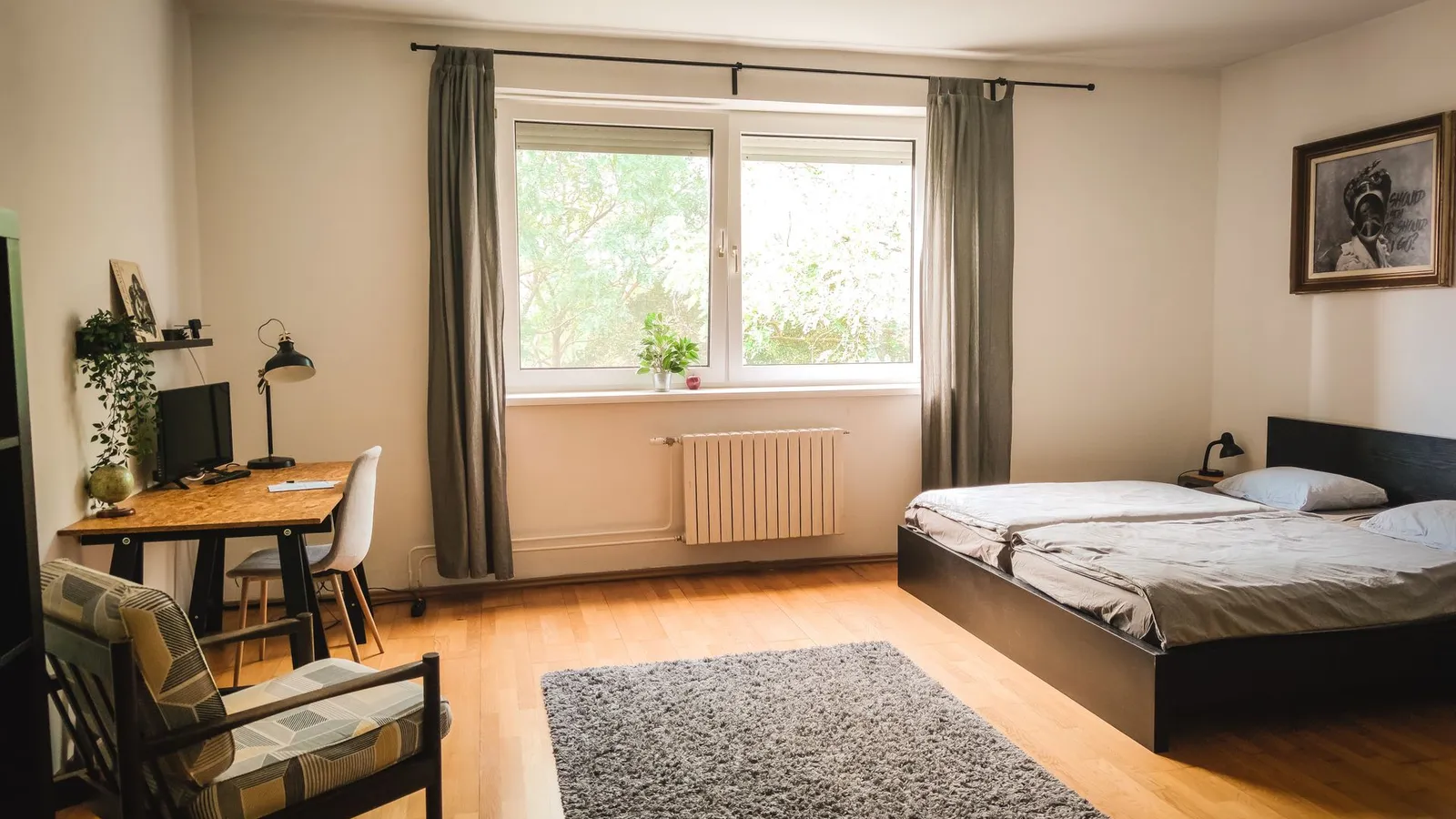 A bedroom with a large grey area rug, wooden desk, and armchair beside a window