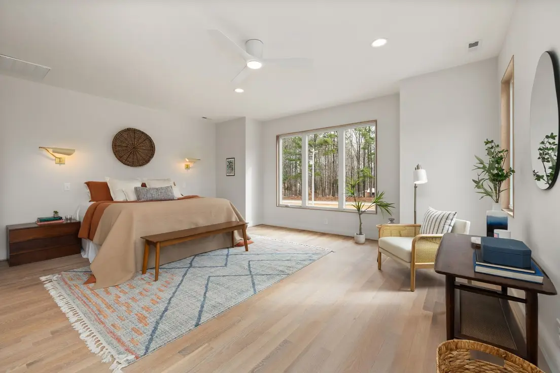 A neutral area rug layered under a bed with a warm terracotta throw and wood floor