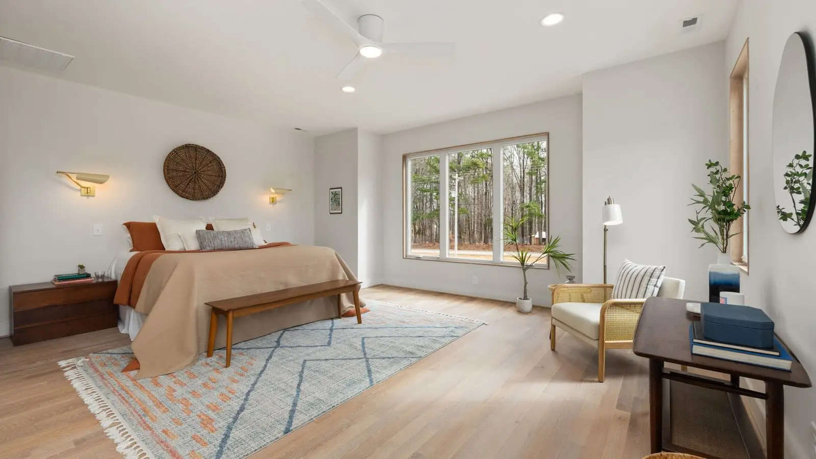 A neutral area rug layered under a bed with a warm terracotta throw and wood floor