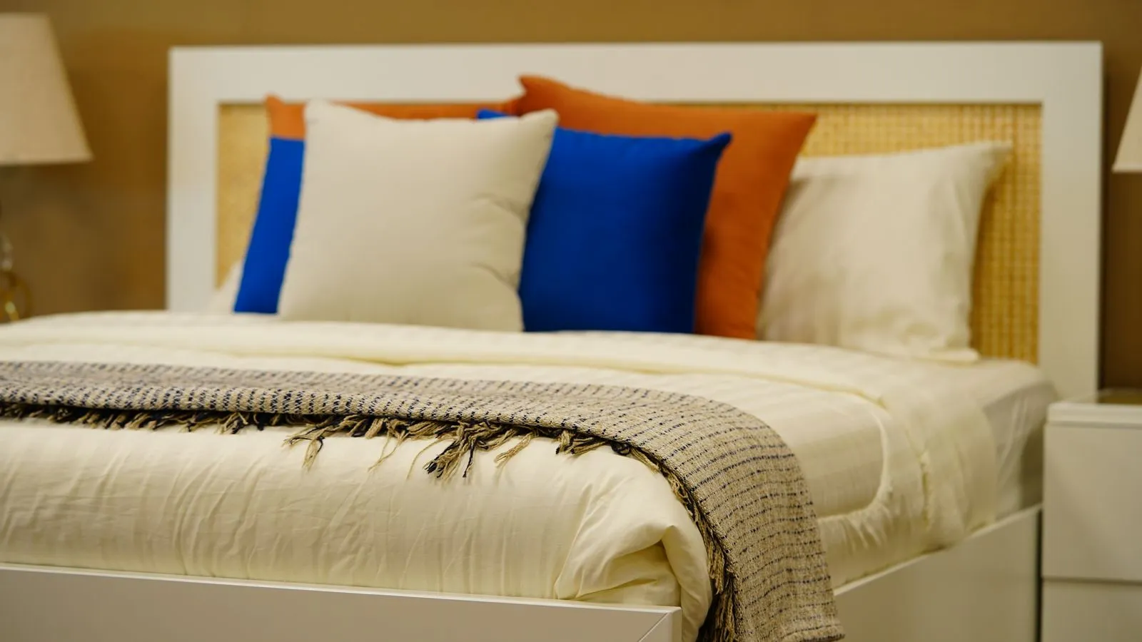 A curated bedroom with cobalt and orange cushions, a cane headboard, and a fringed throw on white bedding