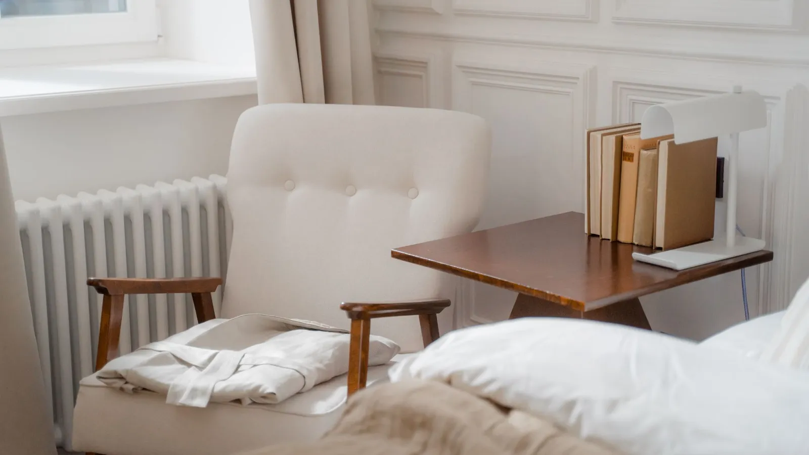 A warm reading nook beside a bed with a stack of books on a small side table