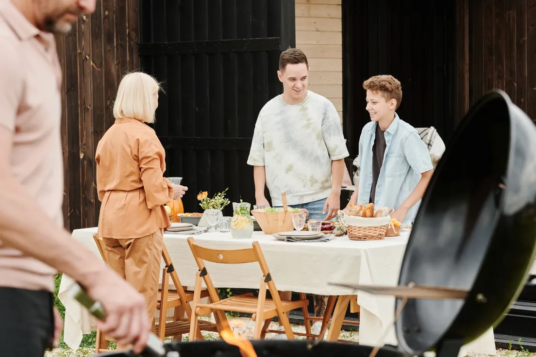 Family gathered around a backyard bbq area grill and dining table