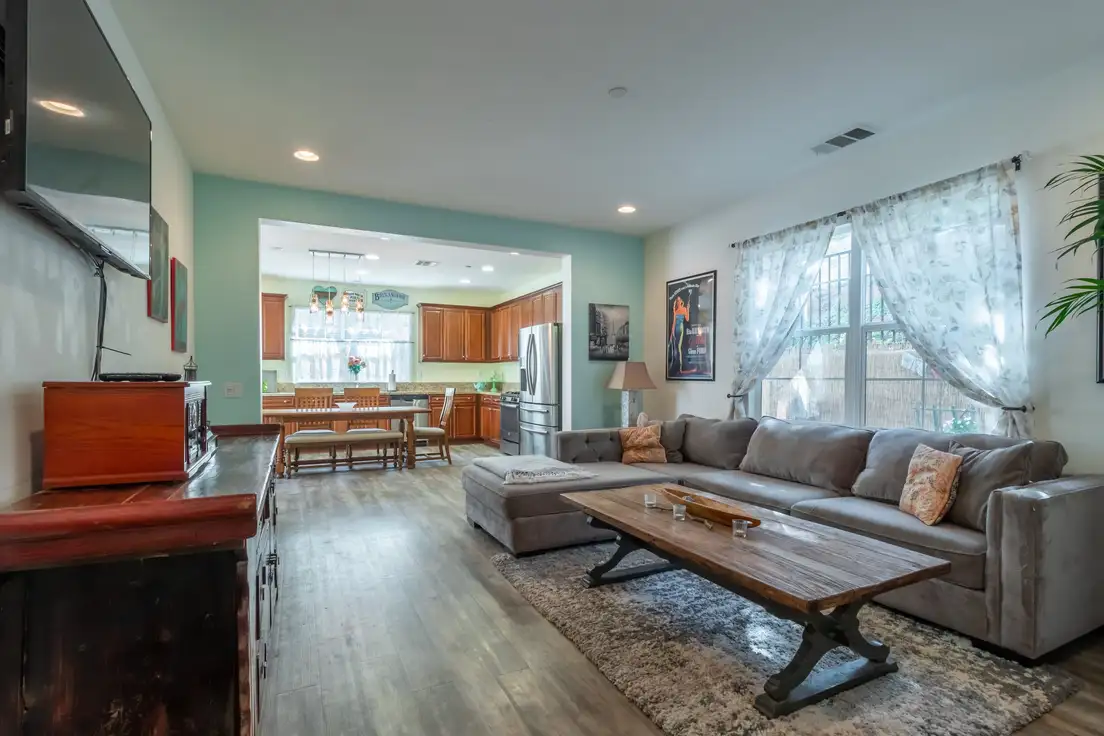 A rustic wooden trestle coffee table in front of a modern gray sectional in an open-concept living room, mixing rustic and modern farmhouse pieces