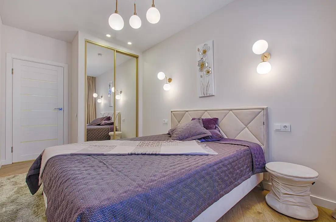 Two wall sconces flanking a bed on either side of a headboard in a small bedroom