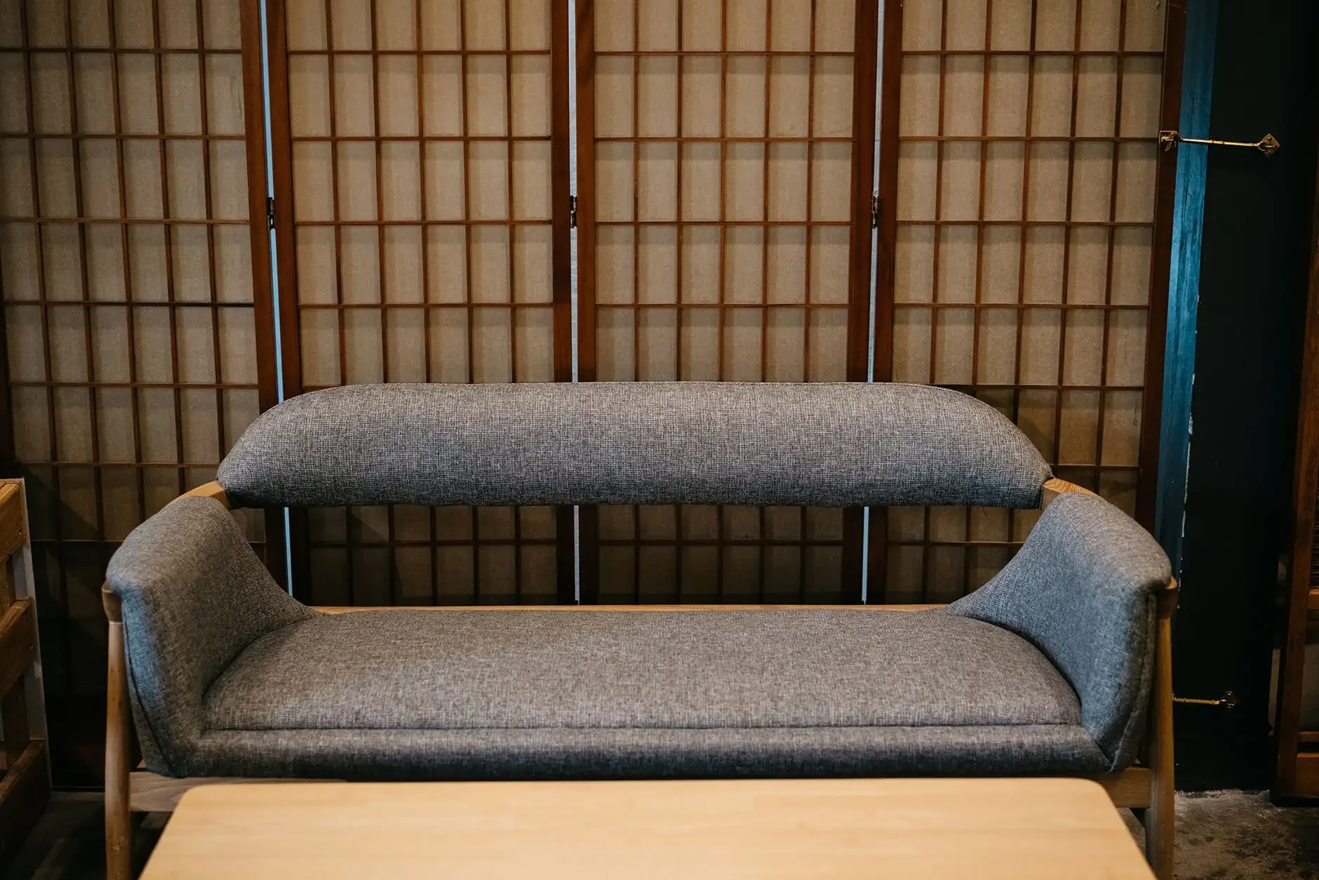 A wood-framed folding screen standing behind a gray sofa, a room divider that separates the living area from a workspace