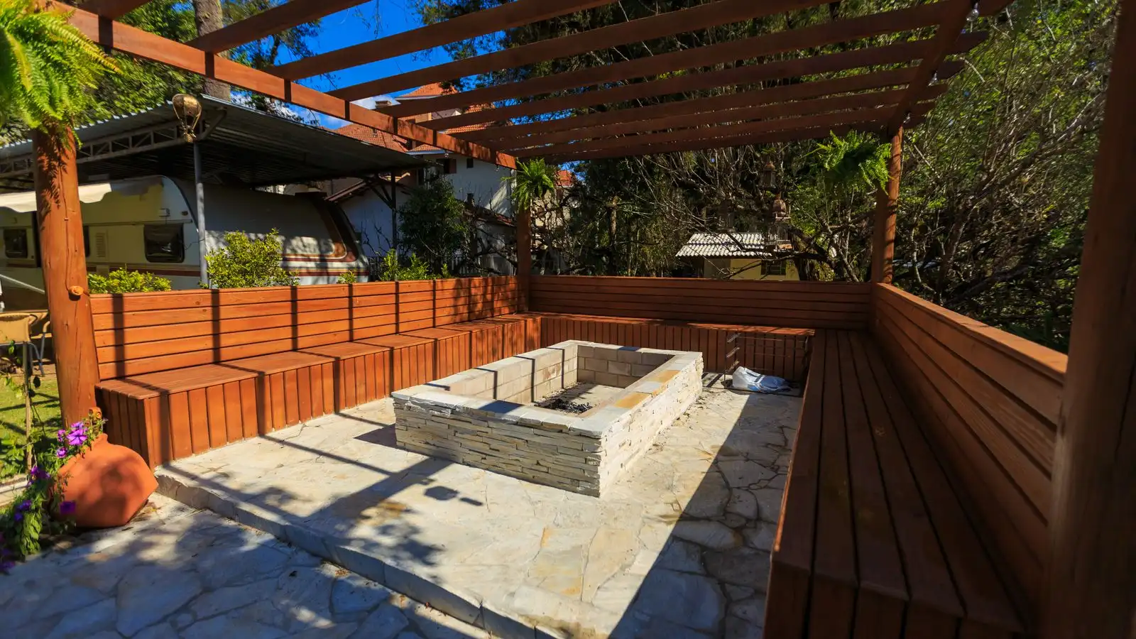 A rectangular stacked-stone fire pit ringed by a built-in cedar bench under a pergola