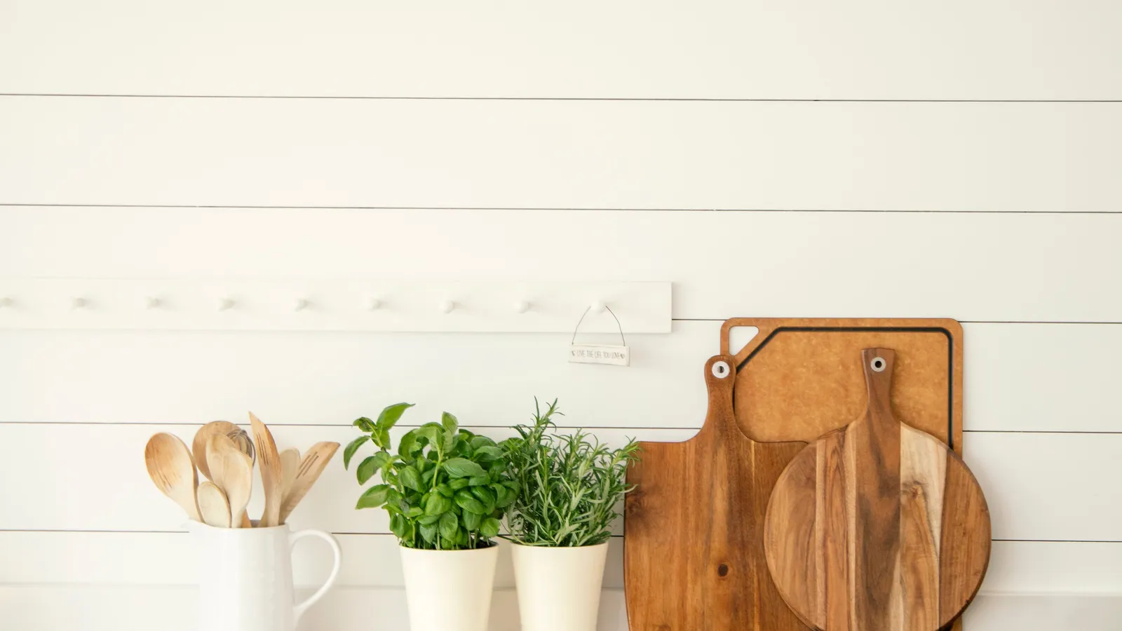 A shiplap kitchen accent wall with wood cutting boards, potted herbs, and a white cabinet