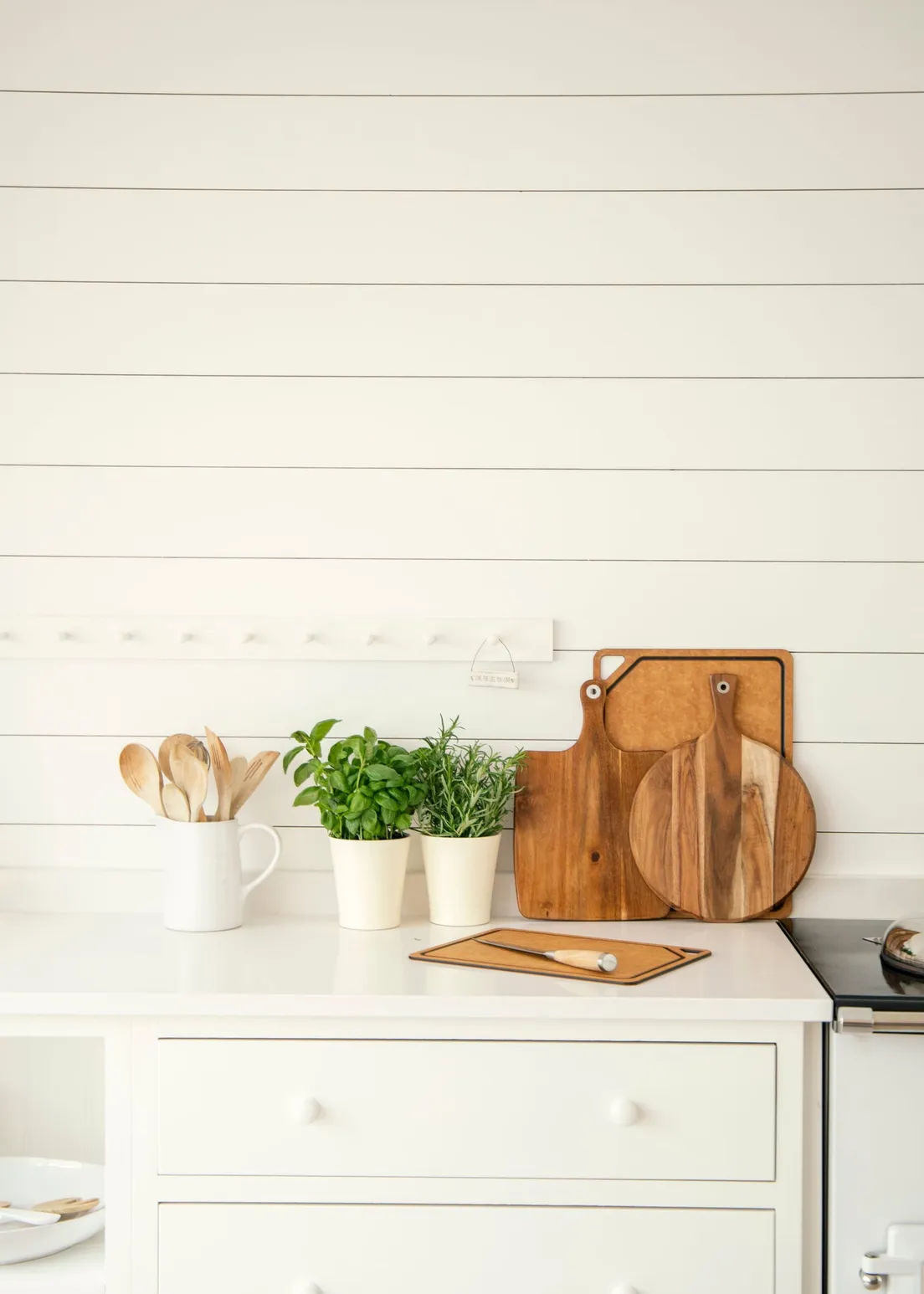 A shiplap kitchen accent wall with wood cutting boards, potted herbs, and a white cabinet