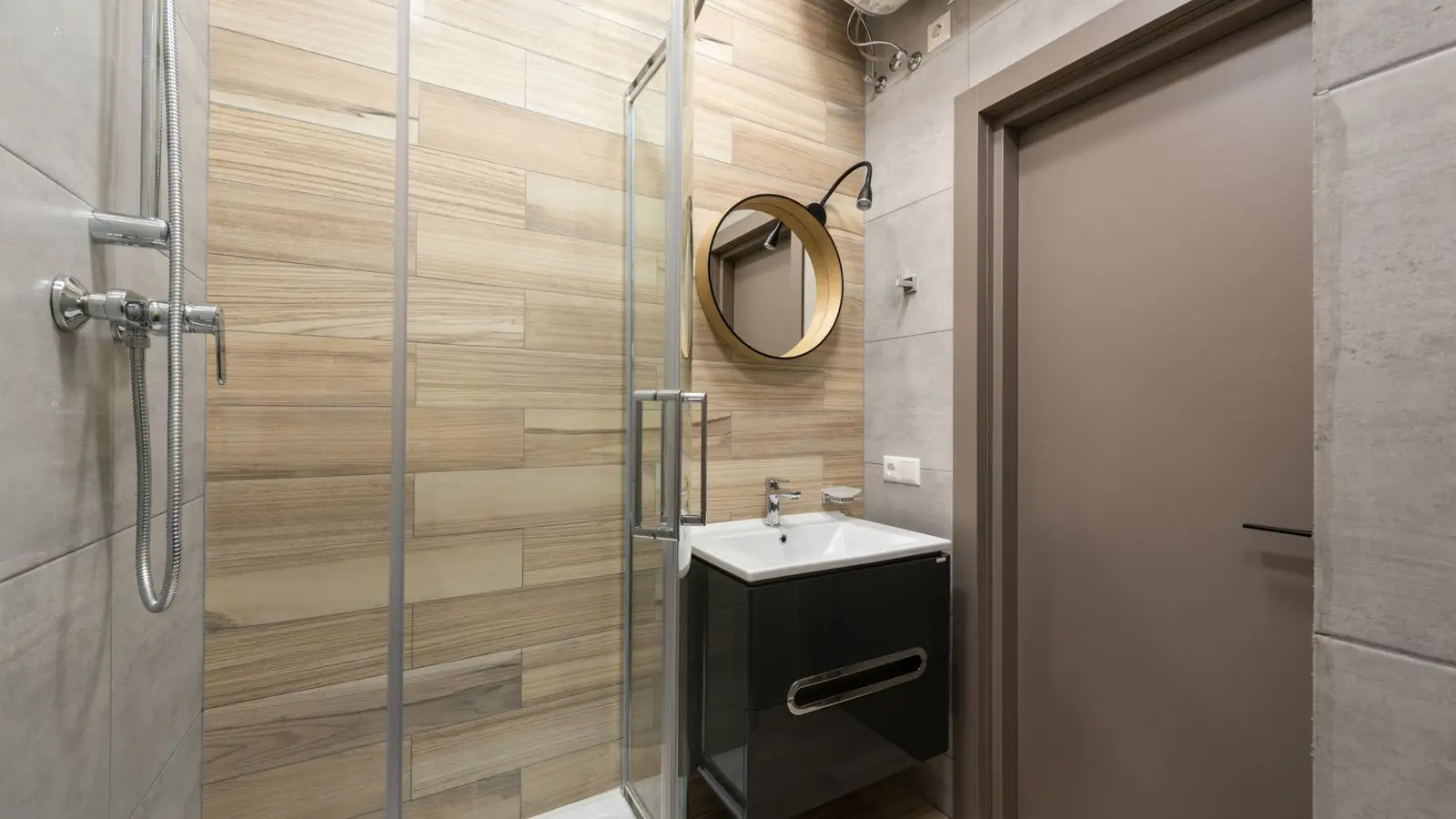 A small bathroom shower with a clear glass door and warm wood-look tile