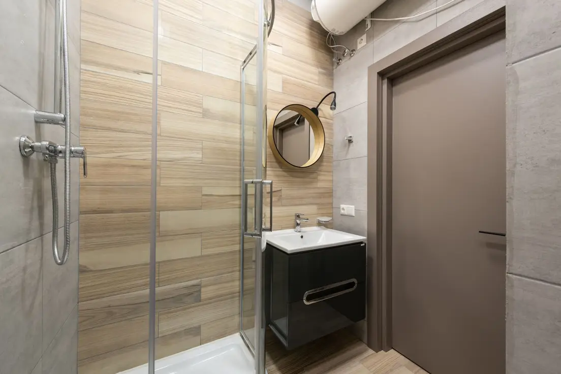 A small bathroom shower with a clear glass door and warm wood-look tile