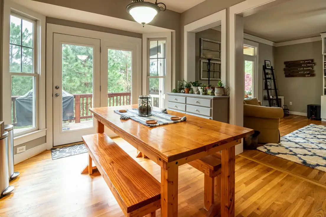 A wood farmhouse dining table and bench next to a painted sideboard dresser, with the living room and area rug visible through the doorway