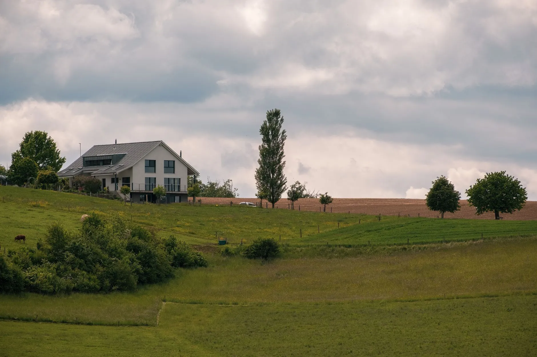 A modern farmhouse exterior in a warm white siding color set in a green countryside