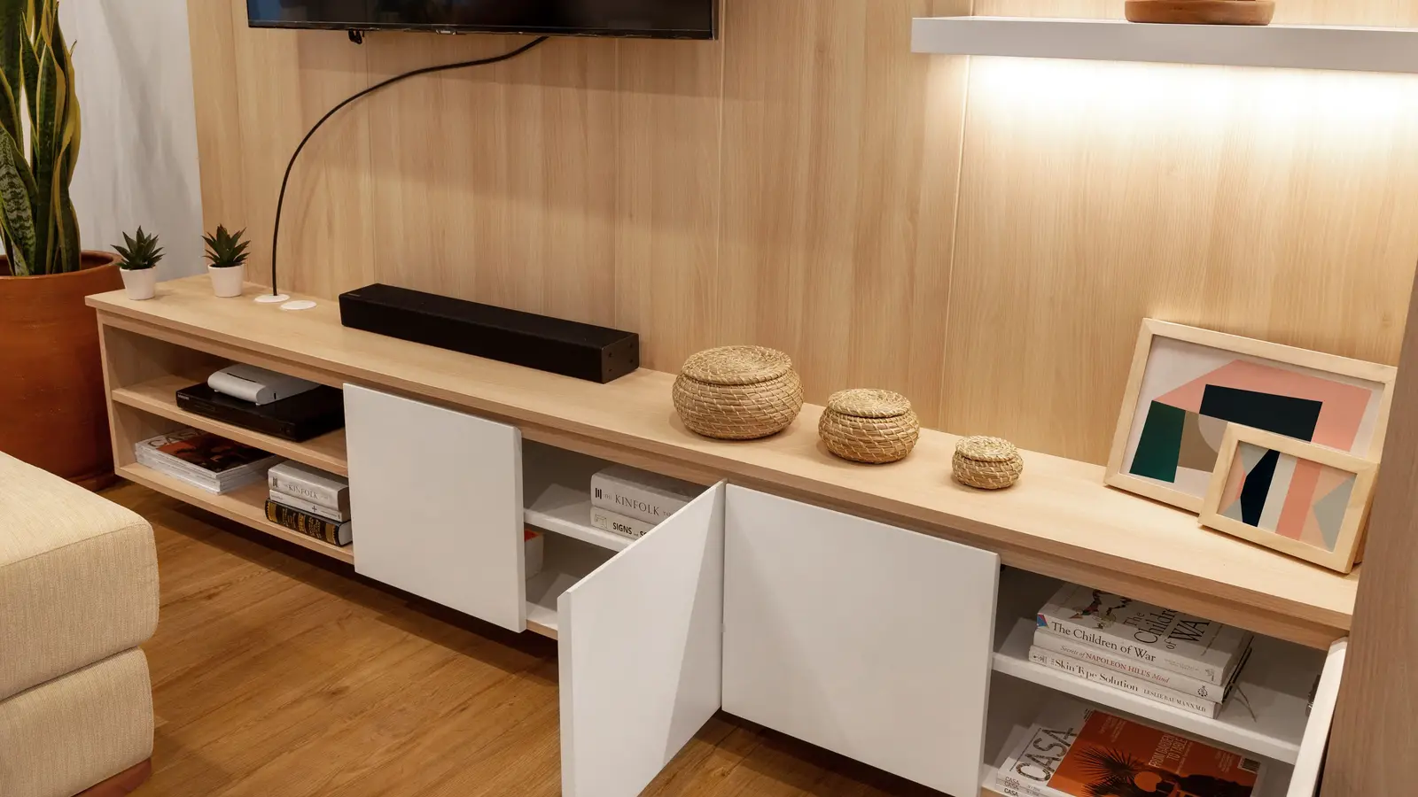 A TV mounted on a wood-paneled accent wall above a light wood media console with open shelving