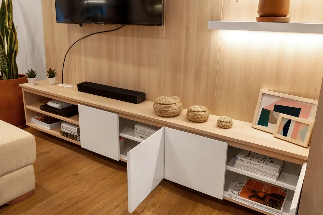 A TV mounted on a wood-paneled accent wall above a light wood media console with open shelving