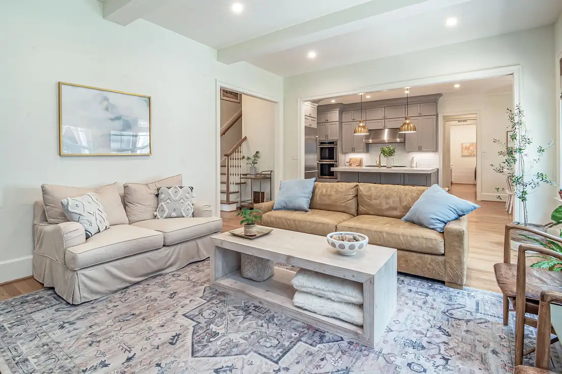 A beige slipcovered loveseat next to a worn leather sofa around a whitewashed wood coffee table on a vintage-style rug