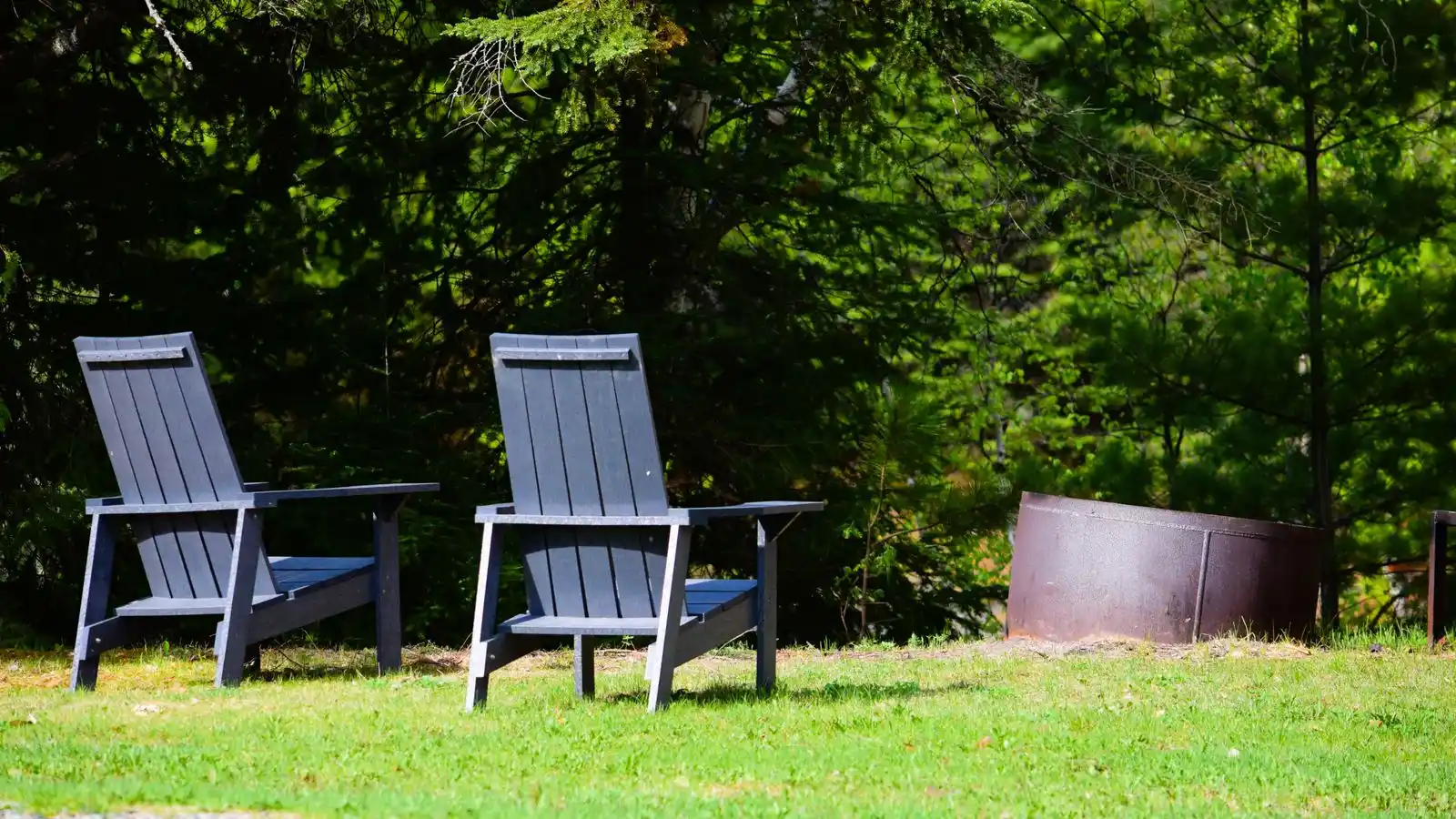 Two modern Adirondack chairs beside a small corrugated-metal fire pit ring in a compact backyard