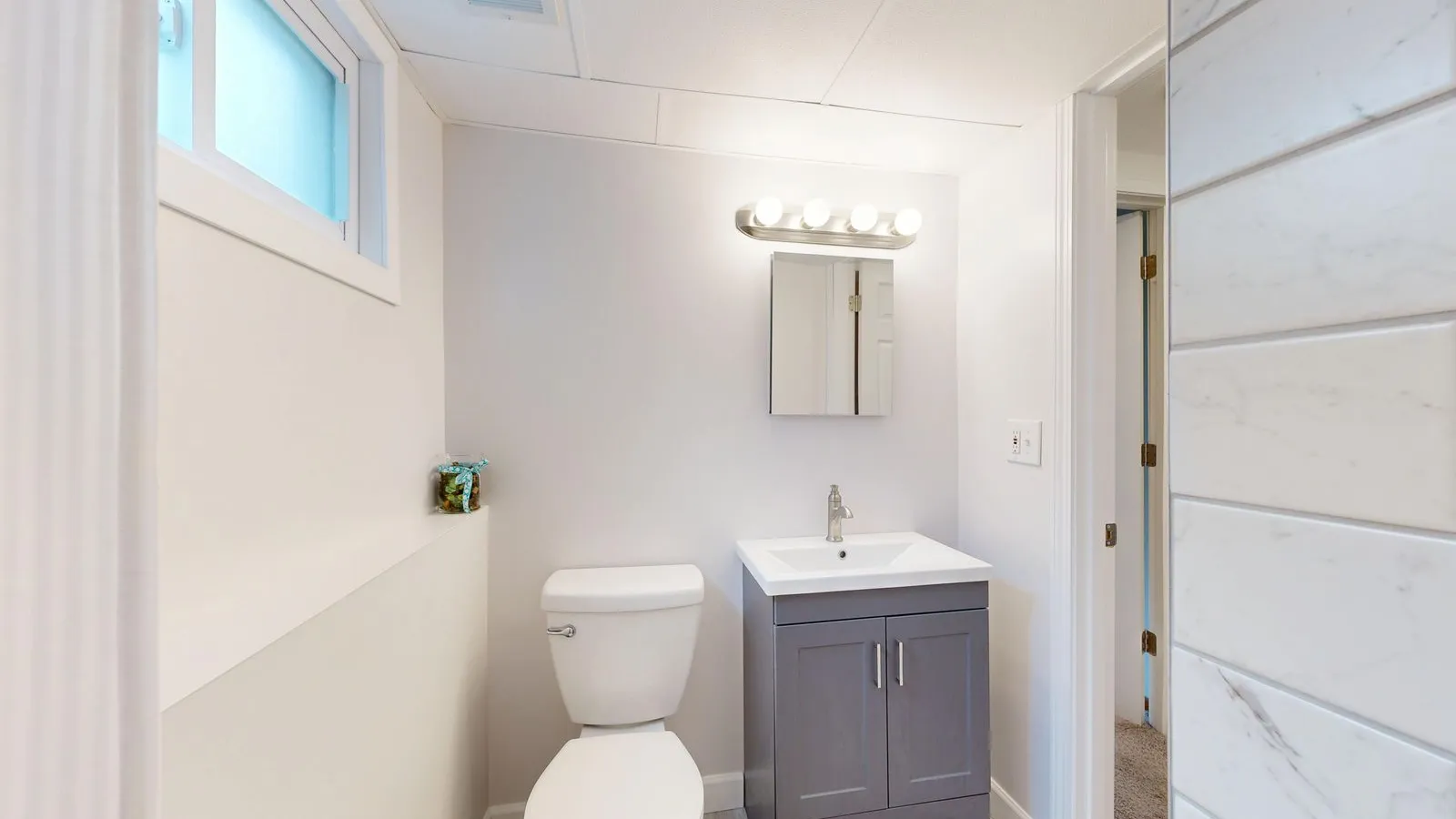 A compact powder room with a toilet, small dark vanity, medicine cabinet, and vanity light bar