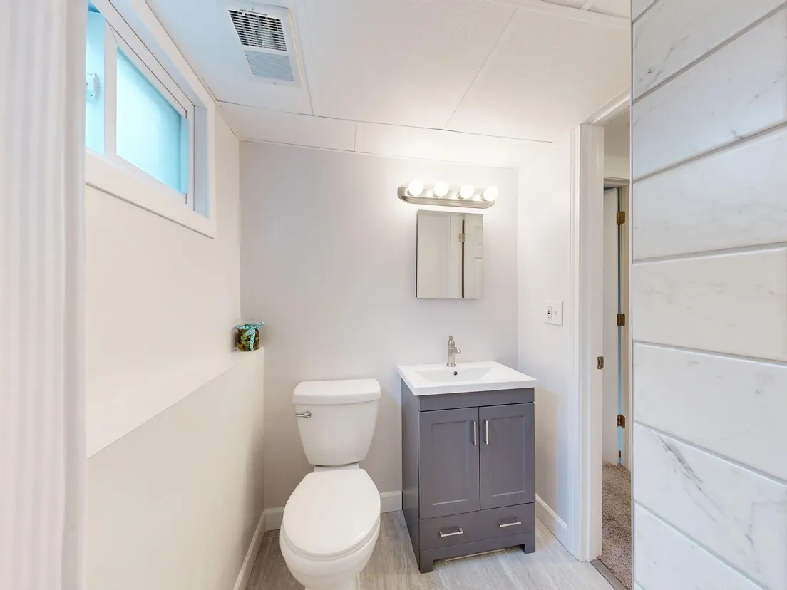 A compact powder room with a toilet, small dark vanity, medicine cabinet, and vanity light bar