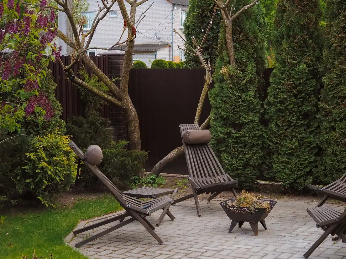 A small backyard paver patio with folding lounge chairs and a fire pit bowl