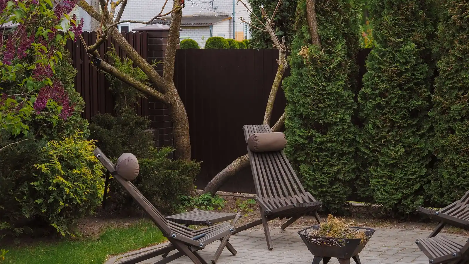 A small backyard paver patio with folding lounge chairs and a fire pit bowl