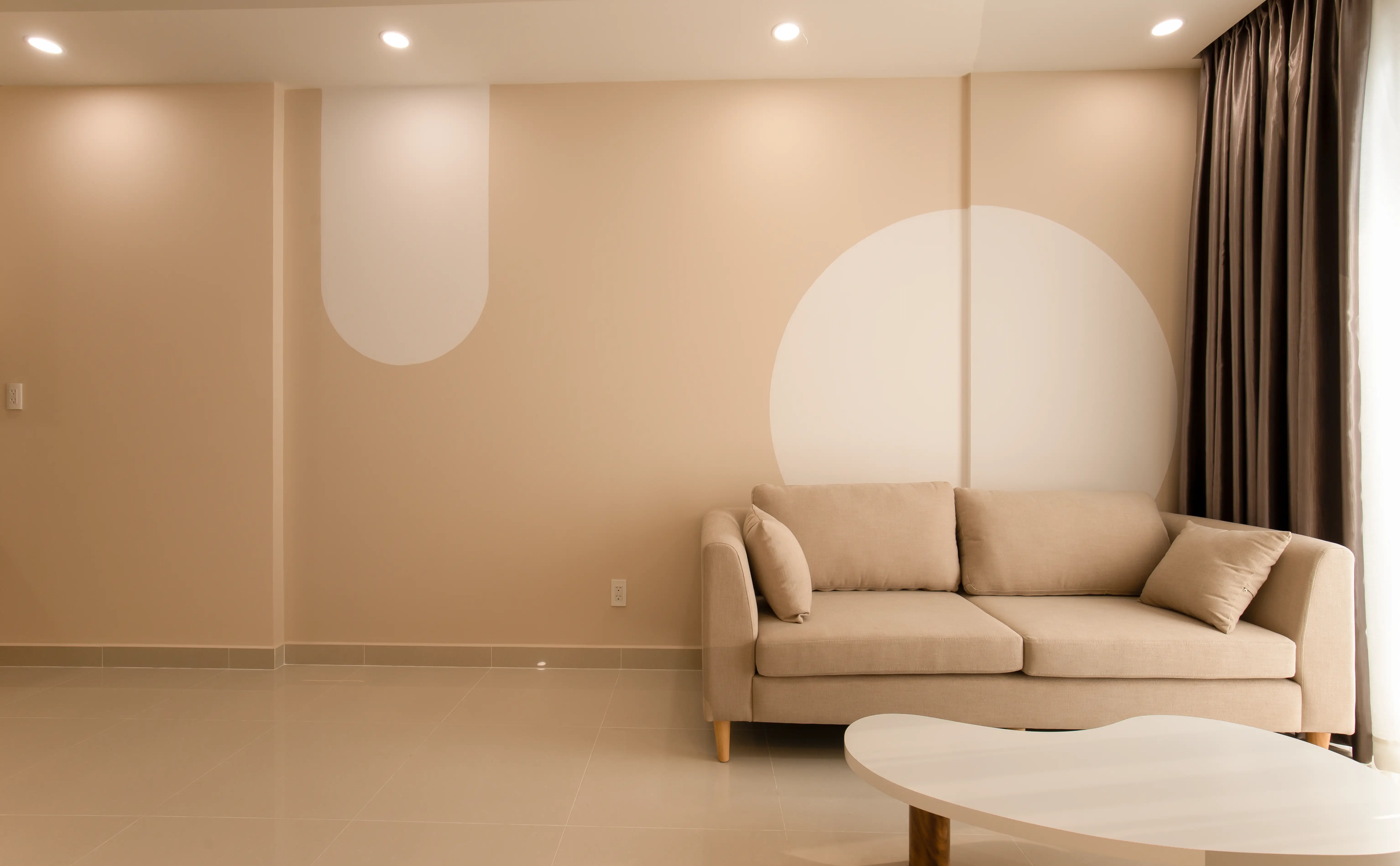 A small minimalist living room with a low beige sofa and neutral decor in a compact apartment