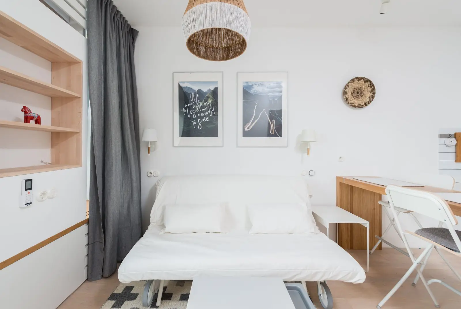 A white fold-out sofa bed in a small studio apartment, opened flat as multifunctional furniture for a guest